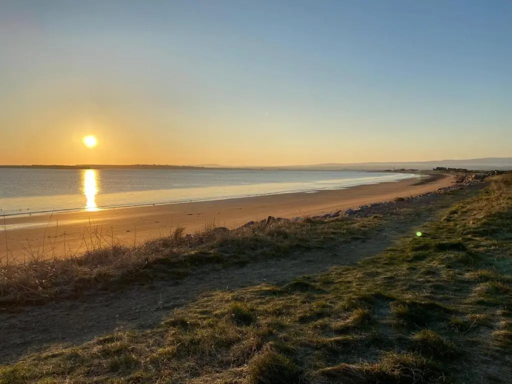 a beach with the sun setting over the water at Stagstone apartment in Fortrose in Fortrose