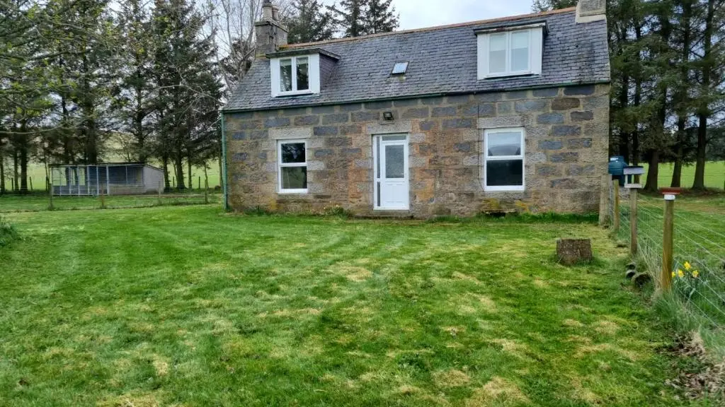 an old stone house with a grass yard at Struan Cottage in Knockandhu