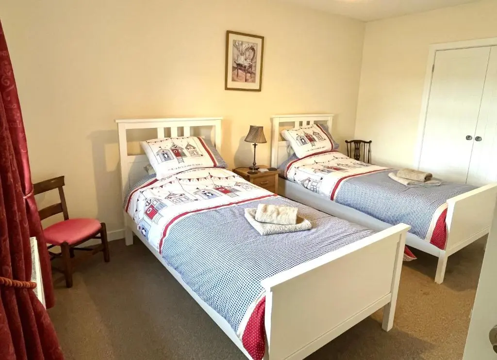 two beds in a bedroom with a red chair and a bed at House By The Sea in Portsoy