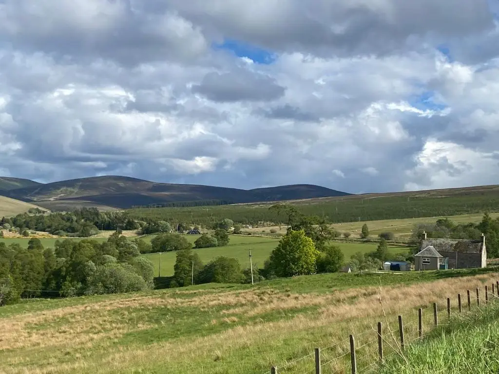 a field with a fence and a house in the distance at Alltachbeg in Tomintoul