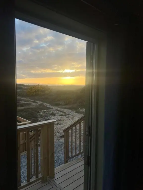 an open door to a balcony with a view of the sunset at Shephards Hut by the Beach in Findhorn