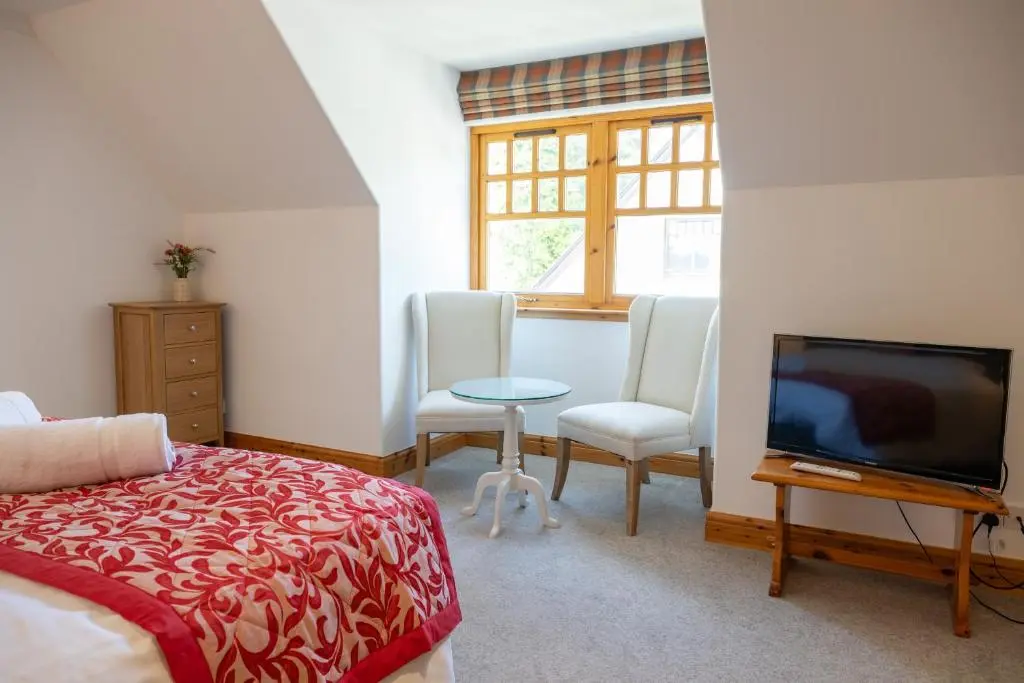 a bedroom with a bed and a tv and chairs at Old Distillery Lodge in Kingussie