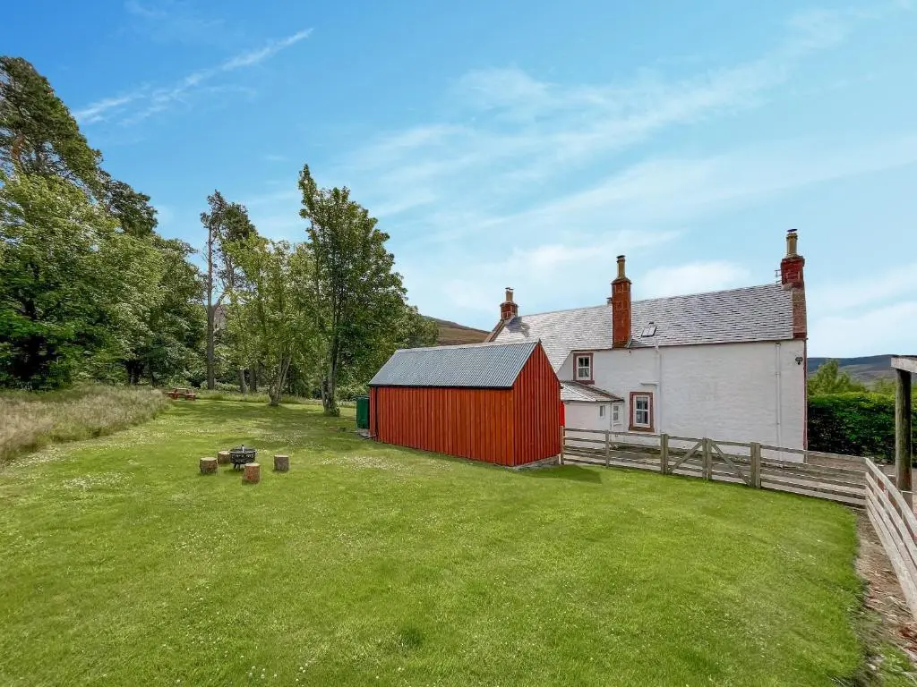 a barn with a red building in a yard at Rottal Farmhouse in Millton of Clova