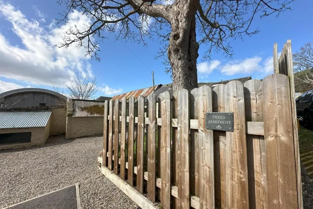 a wooden fence with a sign next to a tree at Tweed Apartment, Golspie in Golspie
