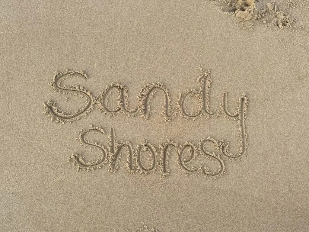 a sign written in the sand on the beach at Sandy Shores in Embo