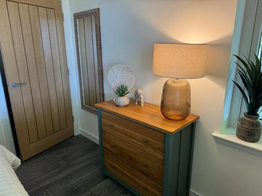 a bedroom with a table with a lamp on a dresser at Wellhouse Country Lodges and Hot Tubs in Tore