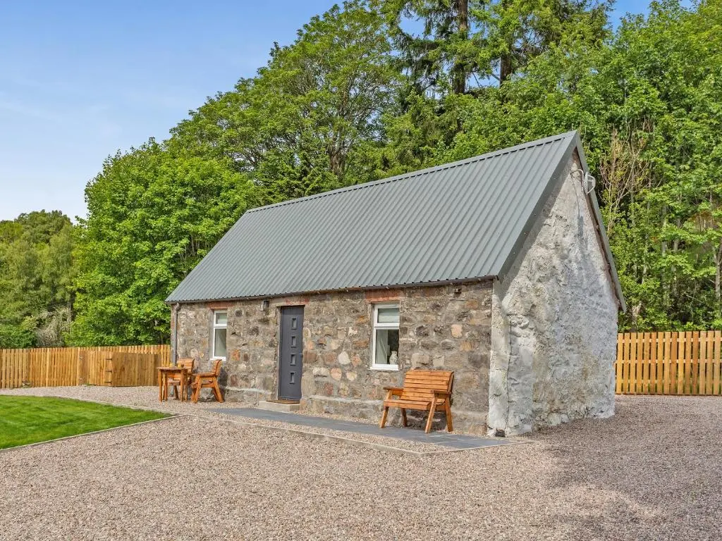 a small stone building with chairs and a fence at Ferry Cottage in Eskadale