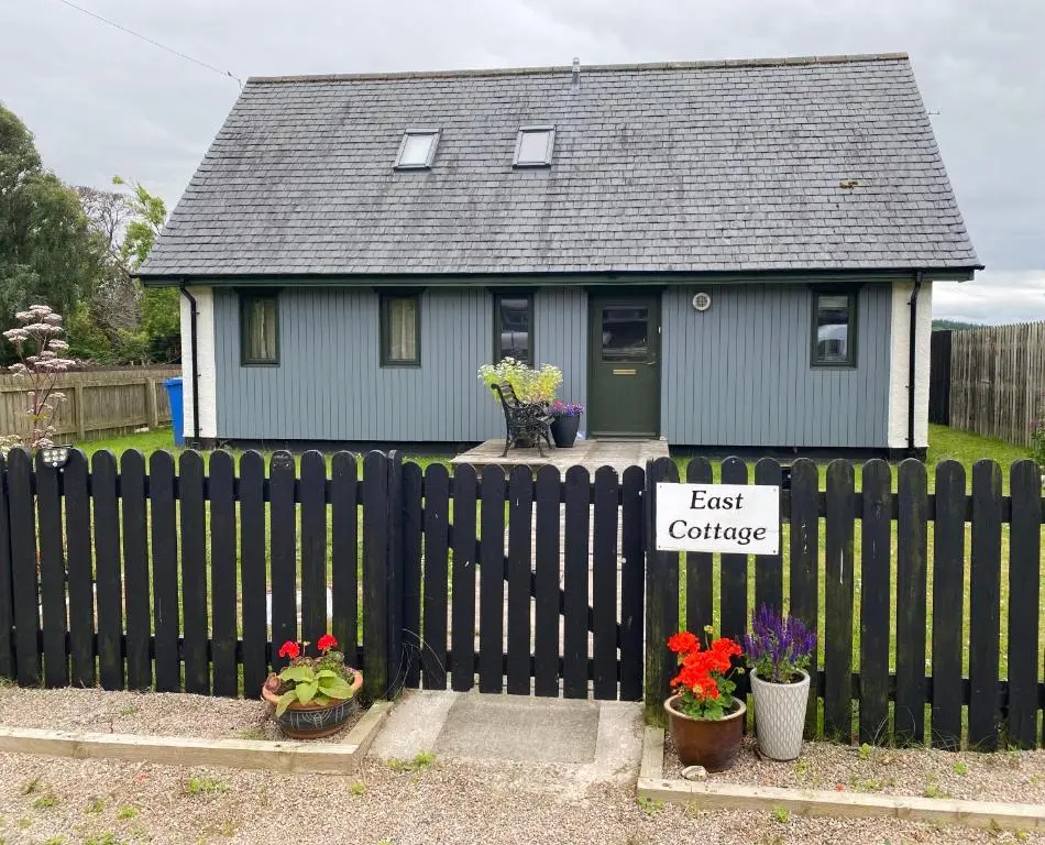 a small house with a black fence and flowers at East Cottage, Brodie in Dyke