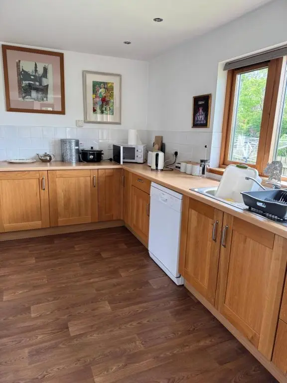 a kitchen with wooden cabinets and a white dishwasher at East Cottage, Brodie in Dyke