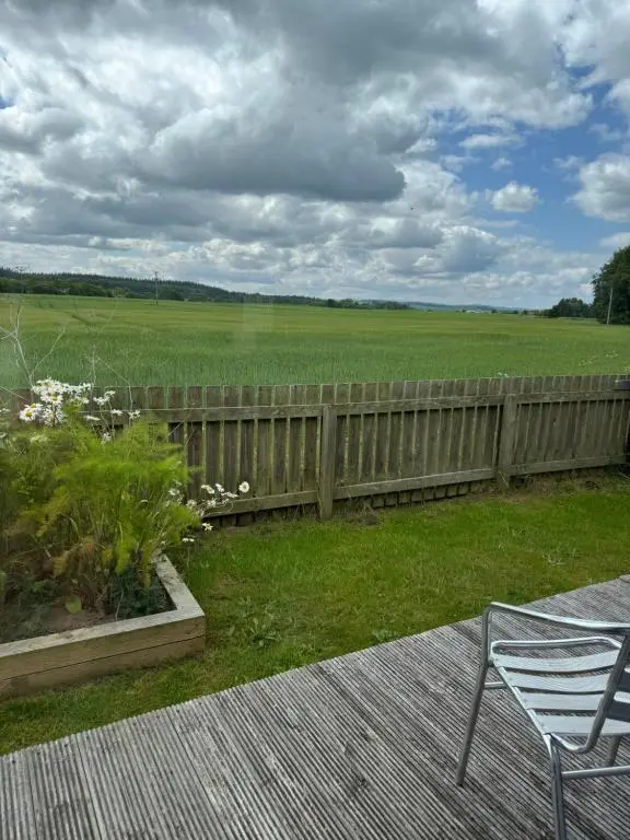 a deck with a chair and a fence and a field at East Cottage, Brodie in Dyke