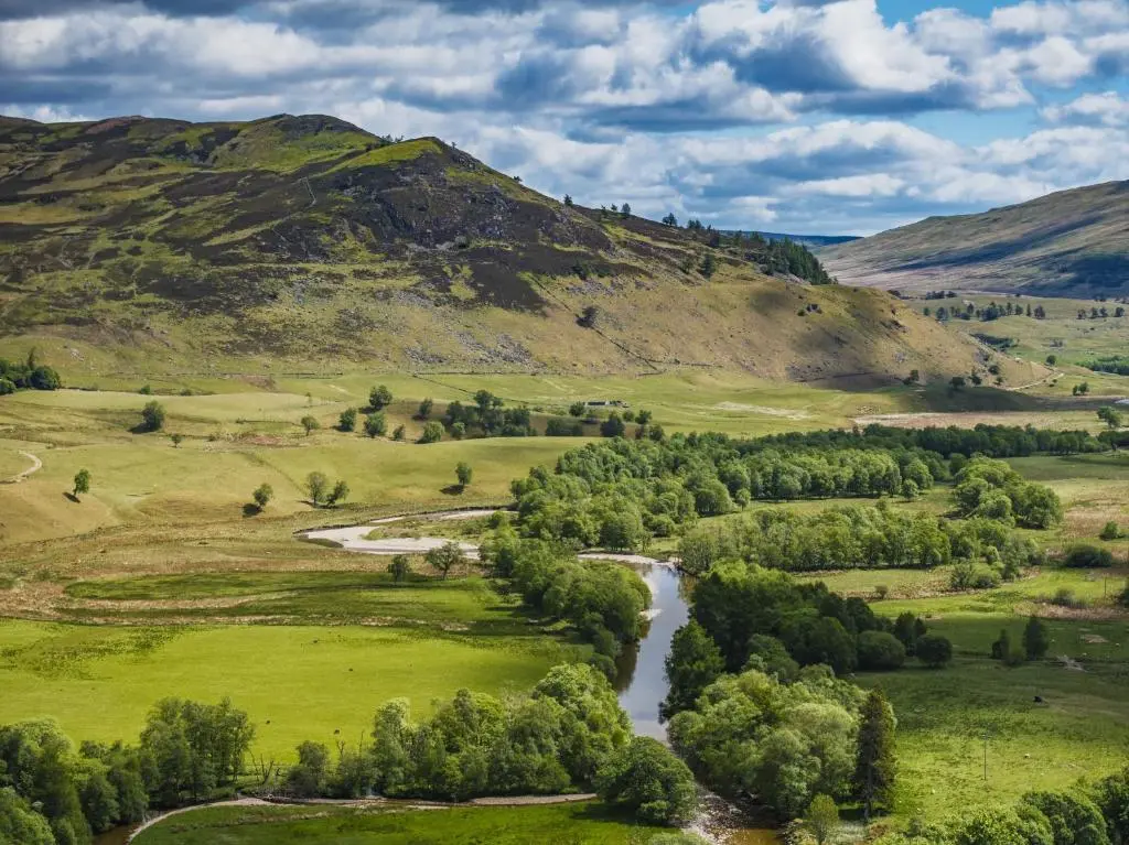 a river in a field with mountains in the background at Finest Retreats - Cragdhu Log Cabin in Glenshee