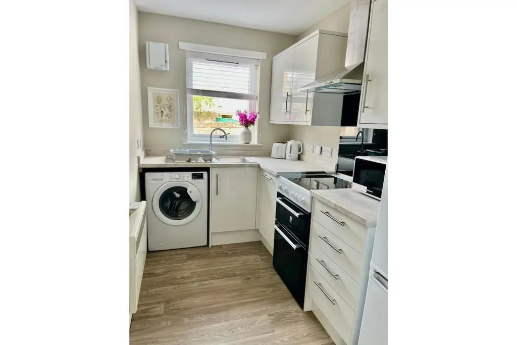a kitchen with white cabinets and a washer and dryer at Flat by the Firth - Stay in the heart of Nairn in Nairn