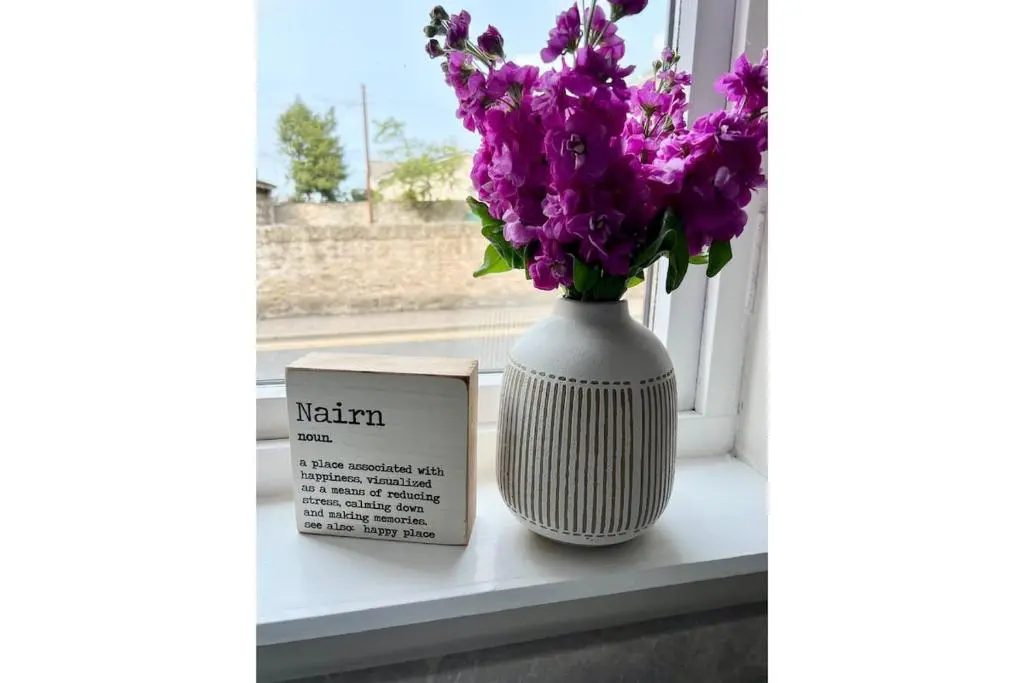 a white vase with purple flowers sitting on a window sill at Flat by the Firth - Stay in the heart of Nairn in Nairn