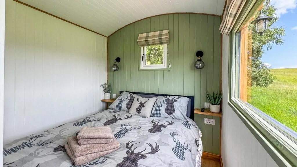 a bed in a small room with a window at Cnocvann Croft Shepherd Huts in Kilmorack