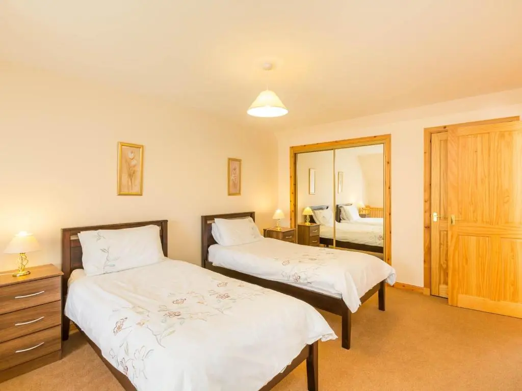 a bedroom with two beds and a mirror at Broombank Cottage in Inverness