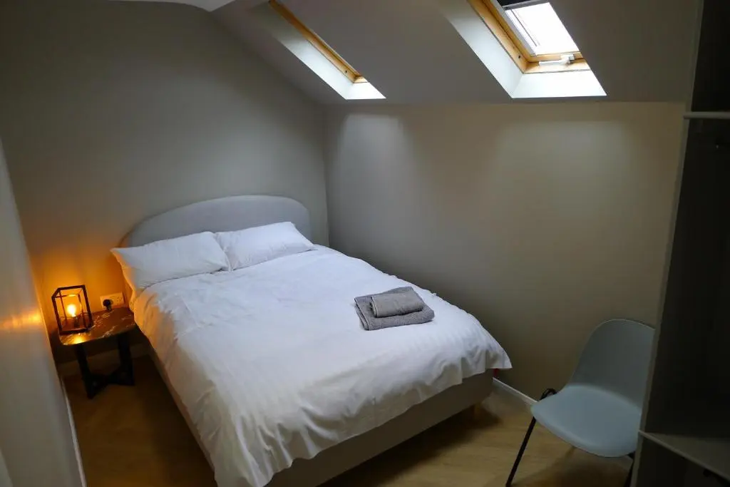 a bedroom with a bed with white sheets and two windows at Hanover st partment in Fraserburgh