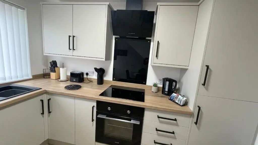 a kitchen with white cabinets and a black refrigerator at The Den - by Caithness Luxury Apartments NC500 - 2 Bedroom holiday home - Sleeps Work teams upto 2 & holiday makers upto 4 in Wick