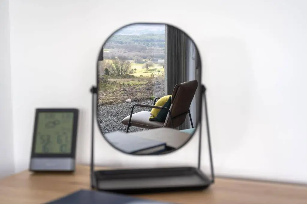 a mirror on a table with a chair and a clock at Migdale Heights - Luxury Cabins in The Highlands in Bonar Bridge