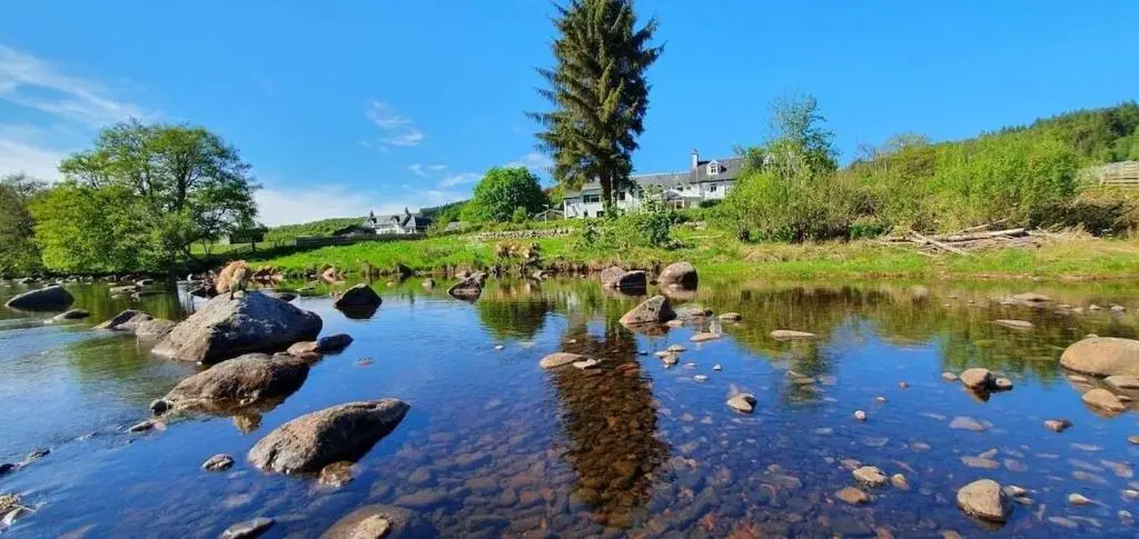 a river with rocks in the water with houses in the background at Tonita in Garve