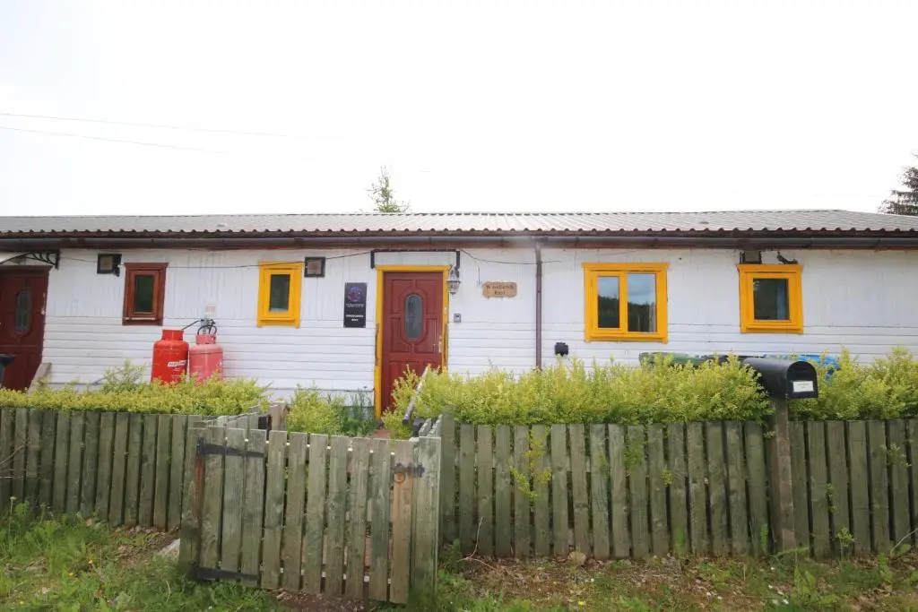 a white house with orange doors and a fence at Woodlands Rest in Garve