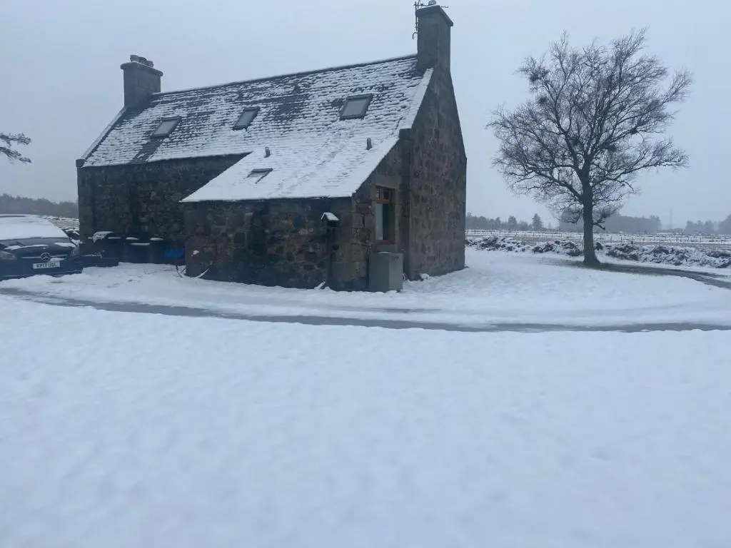 a house covered in snow with a car parked next to it at Cottage Farmhouse in Huntly
