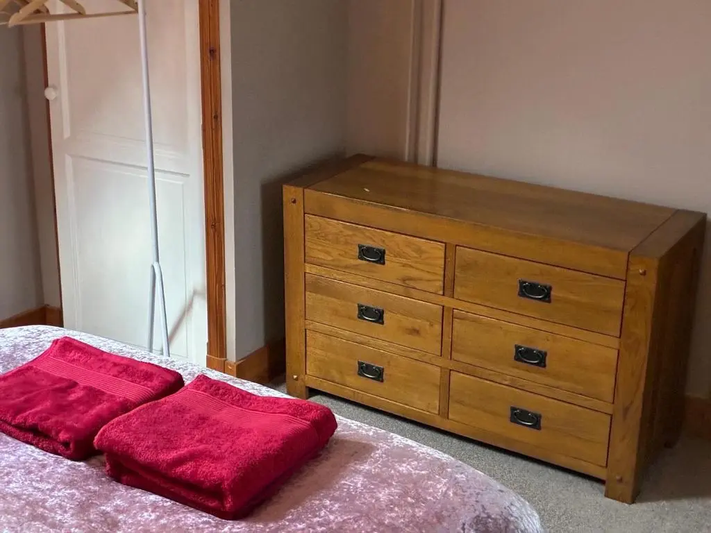a bedroom with a dresser and a red pillow on a bed at Cottage Farmhouse in Huntly