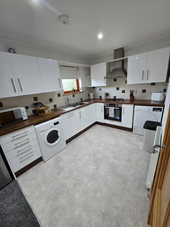 a kitchen with white cabinets and a washer and dryer at Forres Nights in Forres