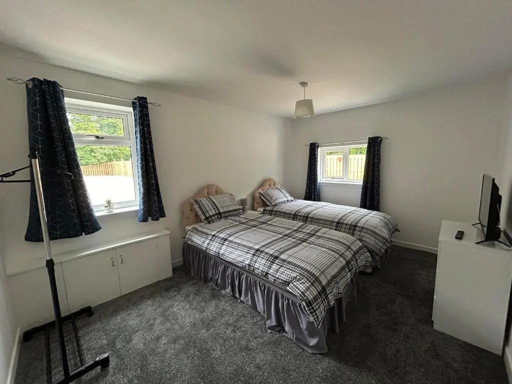 a bedroom with a bed and two windows at Burnside Cottage in Fochabers
