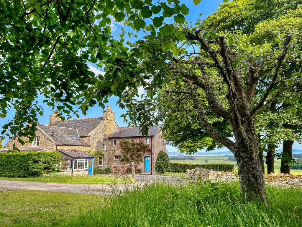 an old stone house with a tree in front of it at The Cottage At Mains House in Tain