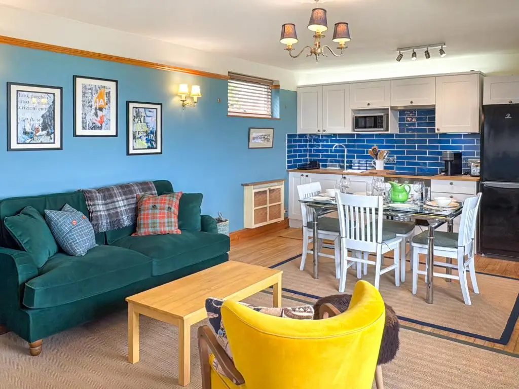 a living room with a green couch and a kitchen at The Cottage At Mains House in Tain