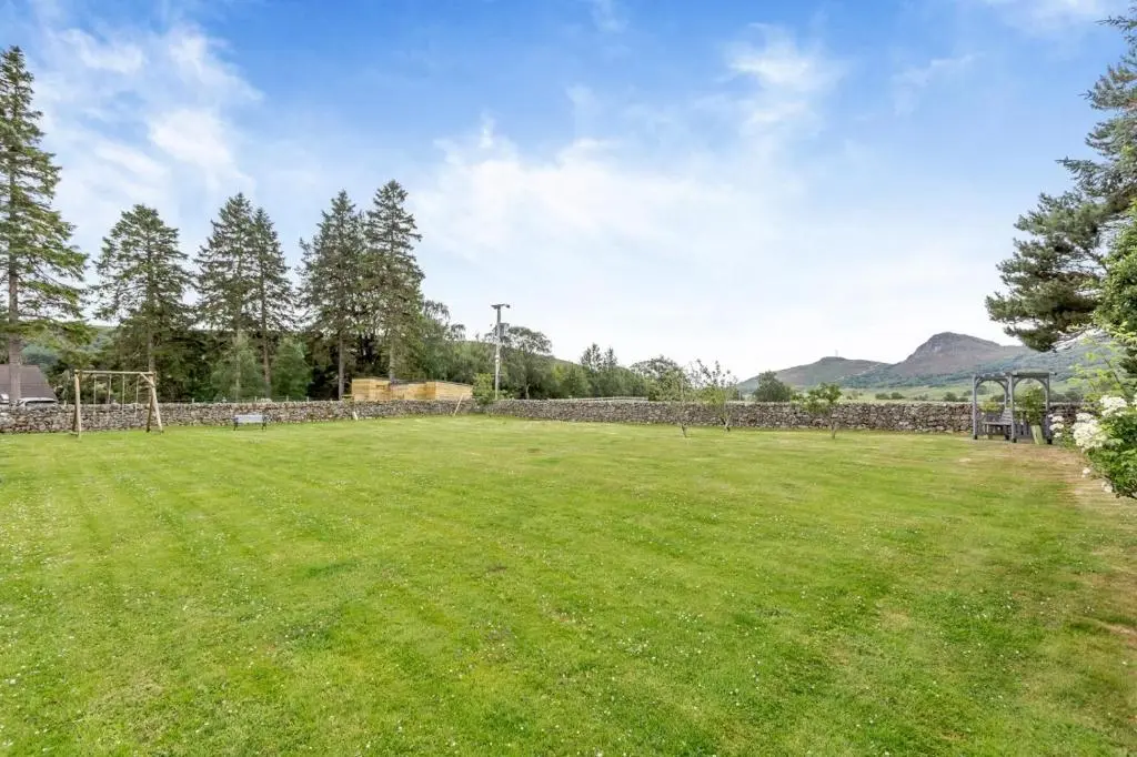 a large grassy field with a stone wall at 1 Bed in Newtonmore oc-l32415 in Newtonmore