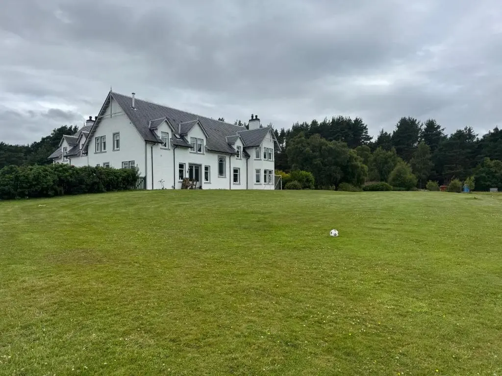 a large white house on a large grass field at Daviot Lodge apartment in Daviot
