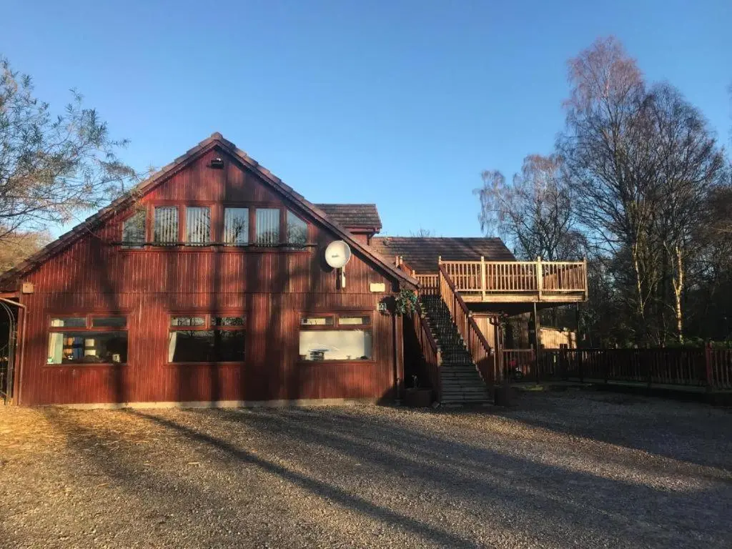 a large wooden house with a deck on the side of it at Cosy Apartment in the Highlands in Muir of Ord