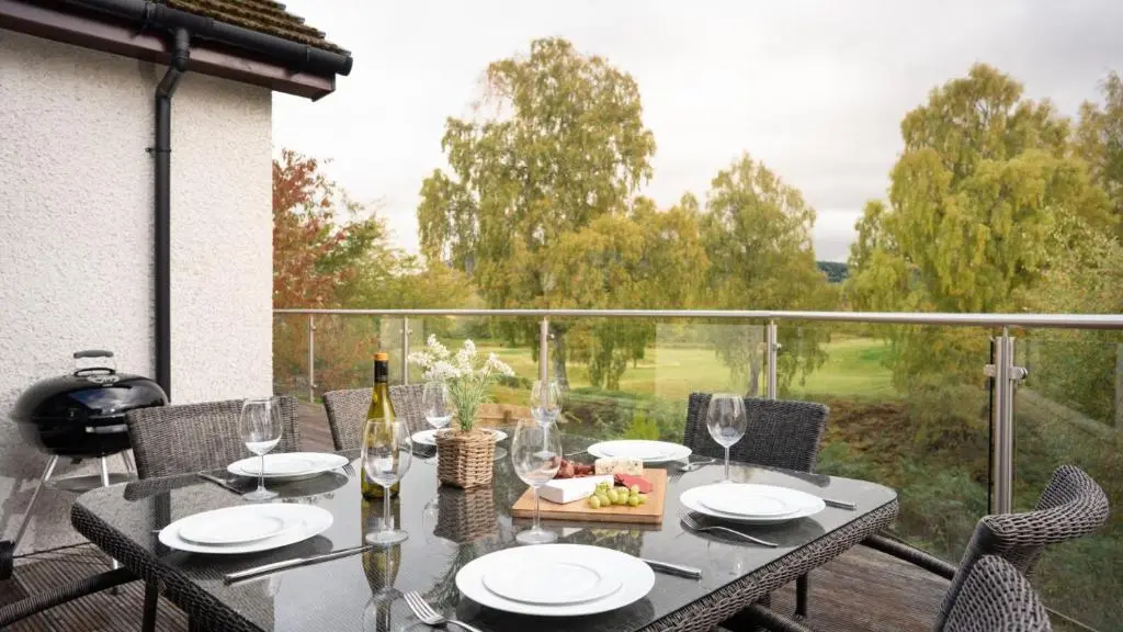 a table with plates and glasses on a balcony at Coorie Lodge in Aviemore