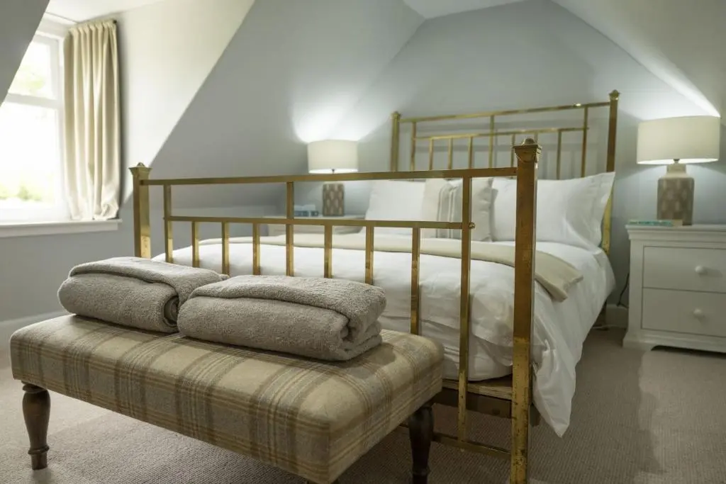 a bedroom with a bed and a bench with towels at Ellon Cottage in Nethy Bridge