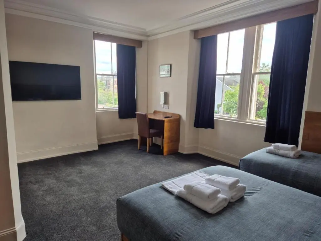 a room with two beds and a desk and windows at Bank House in Inverness
