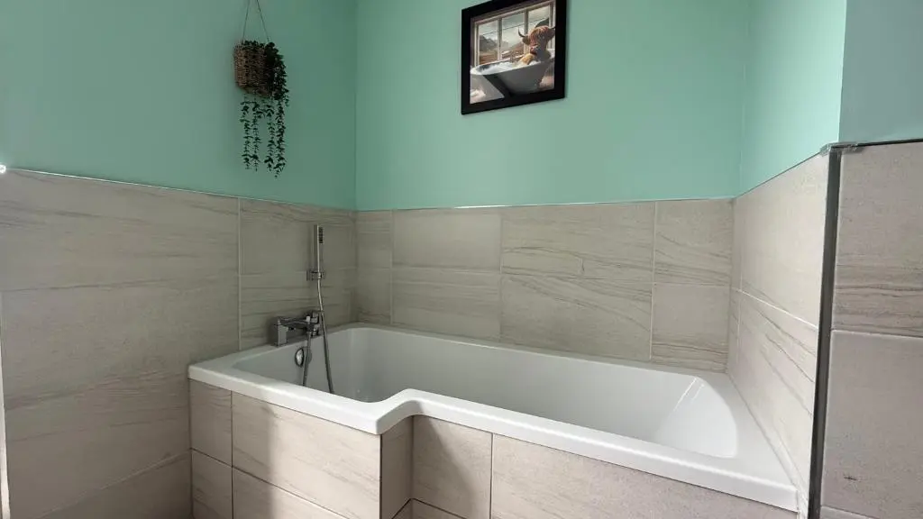 a white tub in a bathroom with a picture on the wall at The Bakehouse - by Caithness Luxury Apartments NC500 - 5 Bedroom Luxury Holiday Home - Sleeps Work teams upto 5 & holiday makers upto 10 in Wick
