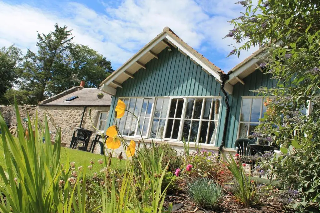 a green cottage with a garden in front of it at St Brandon House Country Cottages in Boyndie