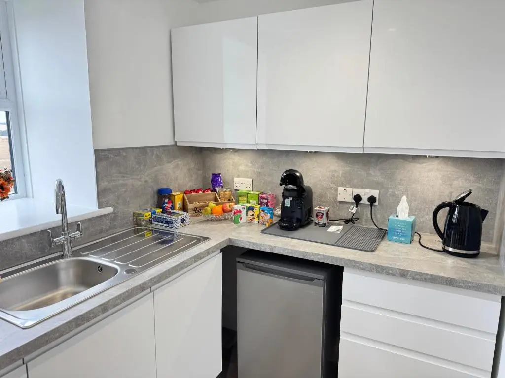a kitchen counter with white cabinets and a sink at Altons Bothy Guest House