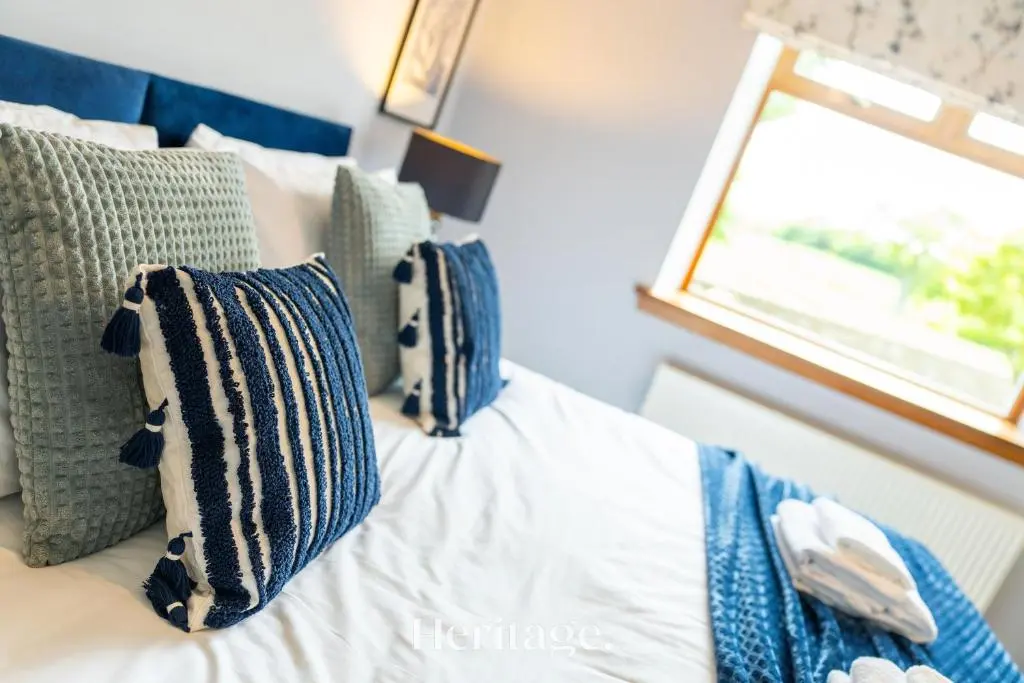 a bed with blue and white pillows and a window at Woodside, Get away with Hot Tub, near Fraserburgh in Strichen