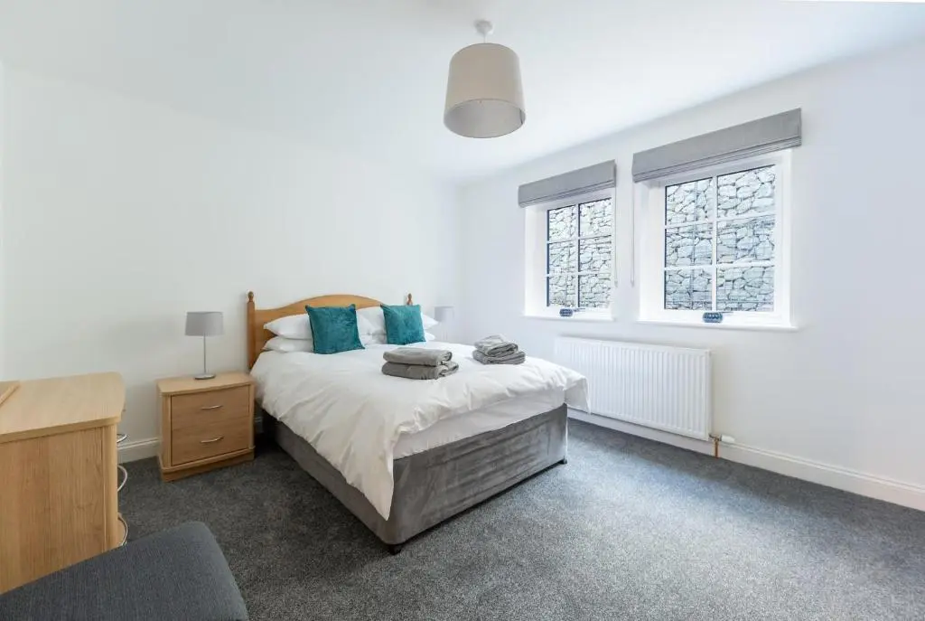a white bedroom with a bed and two windows at Glenview in Tomatin