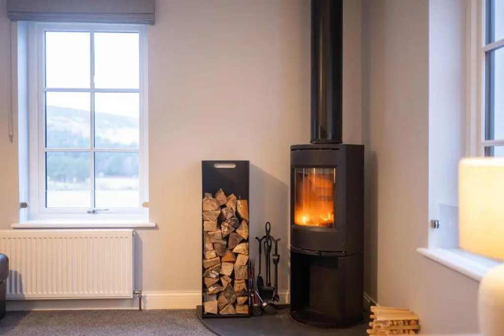 a wood stove in a room with a pile of wood at Glenview in Tomatin