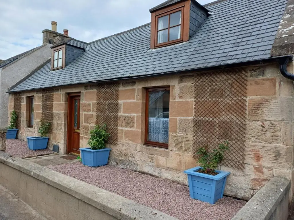 a brick house with three blue plants in front of it at Mary Cottage in Garmouth