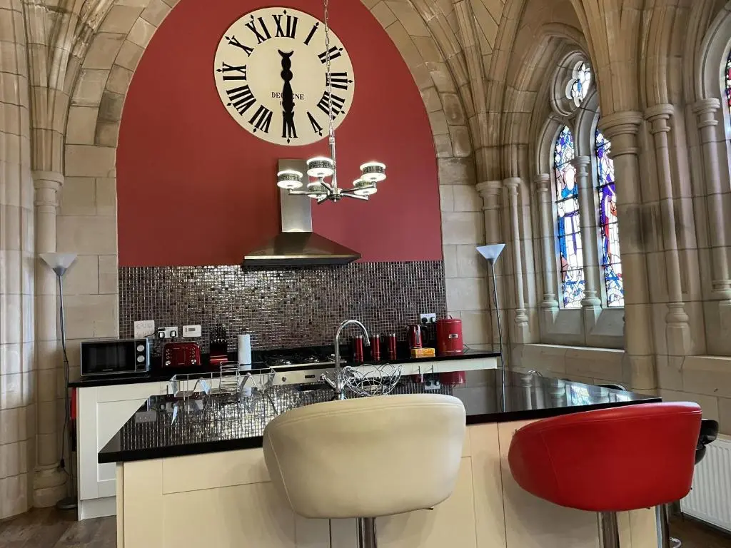 a kitchen with a clock on the wall and two chairs at Romantic getaway at St Andrew's Chapel in Fort Augustus