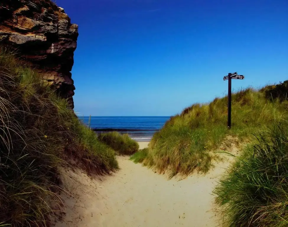 a sandy path leading to a beach with the ocean at Cladach in Lossiemouth