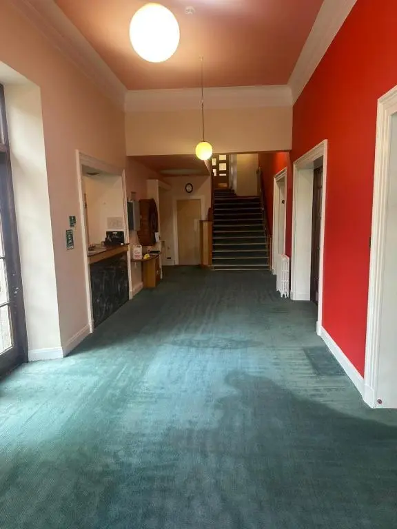 an empty room with a red wall and stairs at Cluny Hill Hotel in Forres