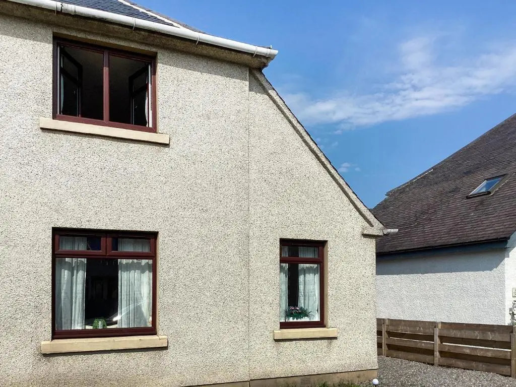 a white house with three windows and a fence at Amayrah Cottage in Inverness