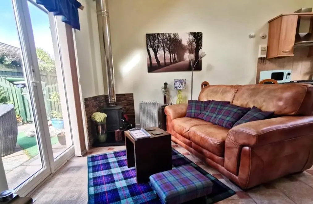 a living room with a brown leather couch and a table at Birch Cottage in Aviemore
