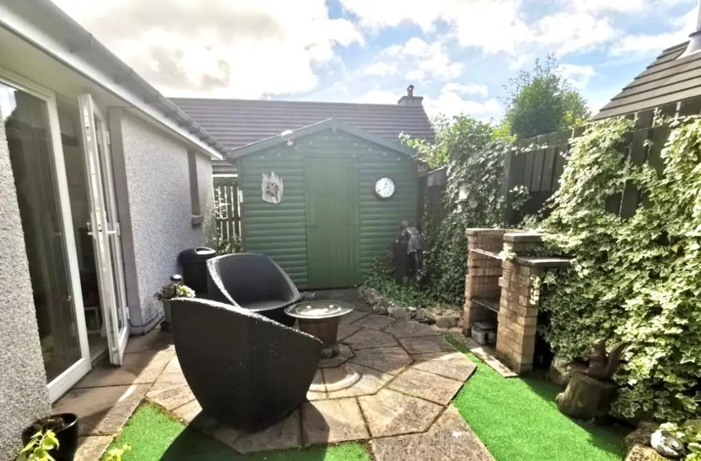 a small backyard with a green shed and grass at Birch Cottage in Aviemore