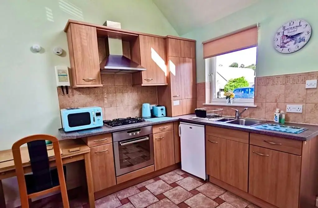 a kitchen with wooden cabinets and a sink and a microwave at Birch Cottage in Aviemore